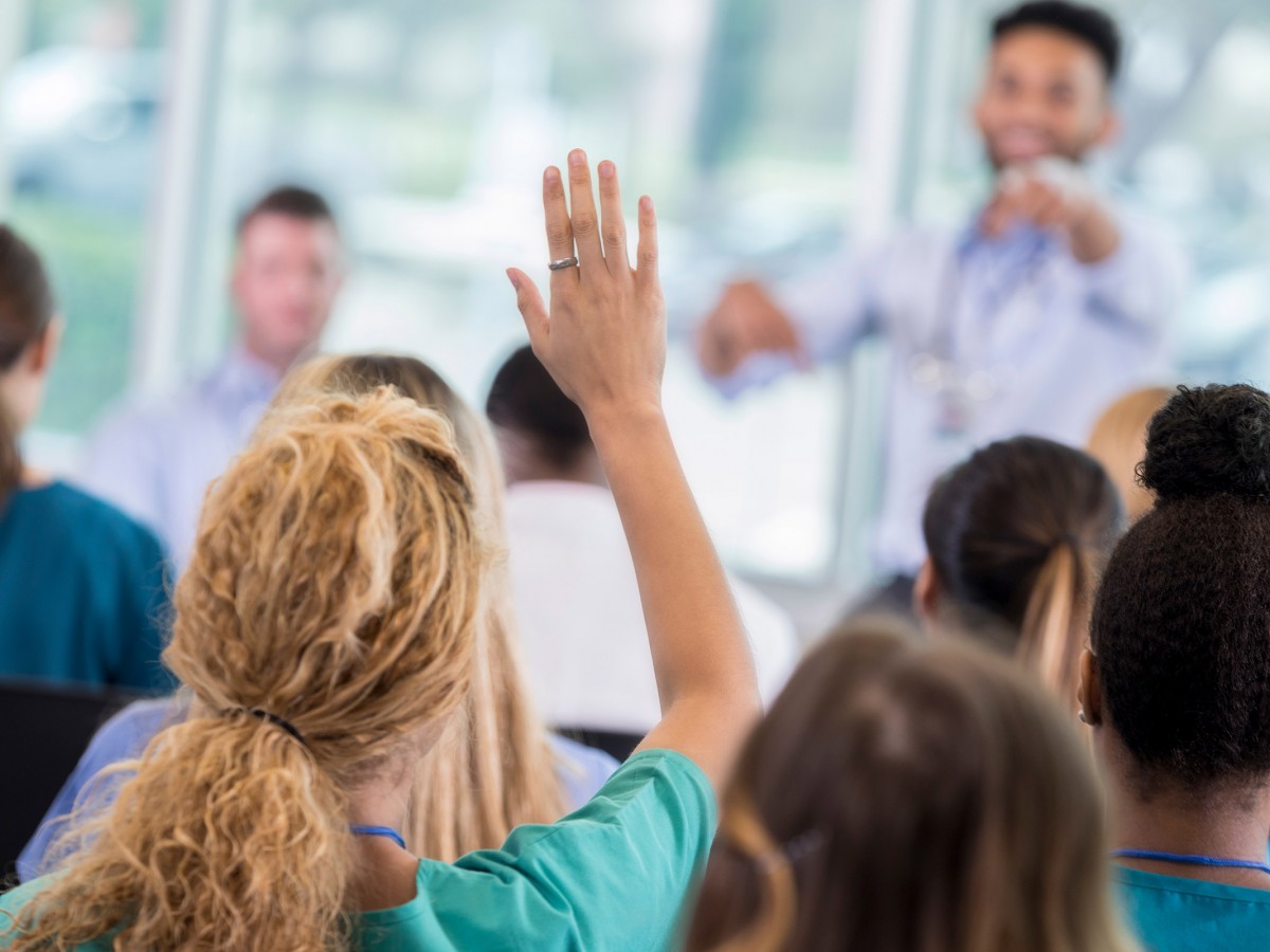 Woman in audience of a speaking event with hand up to ask a question