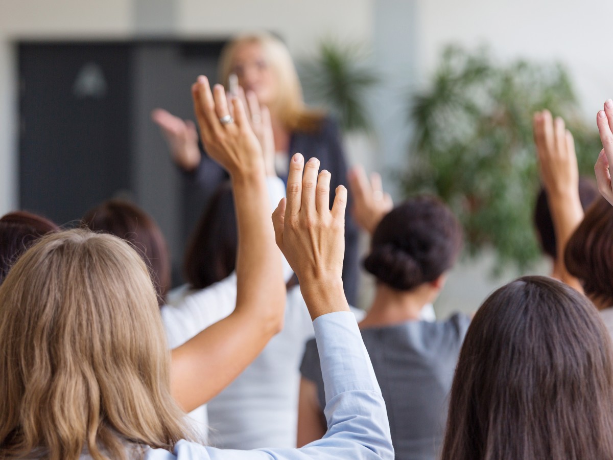 Crowd of people holding their hands up to ask a question