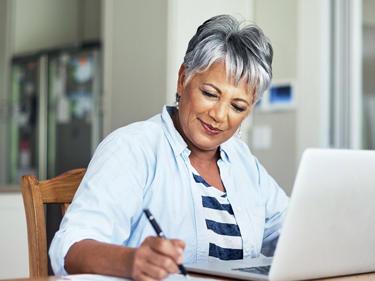 Woman writing notes on notepad while working on laptop