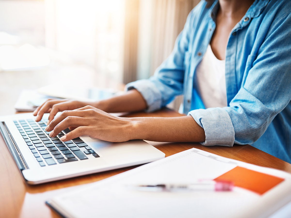 Person sitting at a desk typing on a laptop with notes next to it.