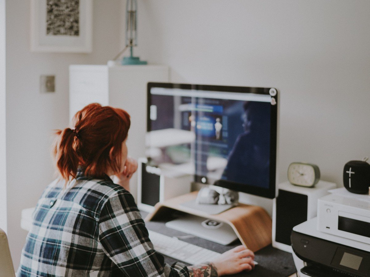 Woman in plaid shirt at desk, in front of large computer display