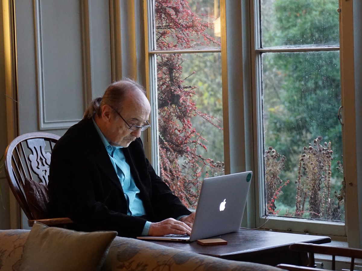 Older man with laptop beside a window