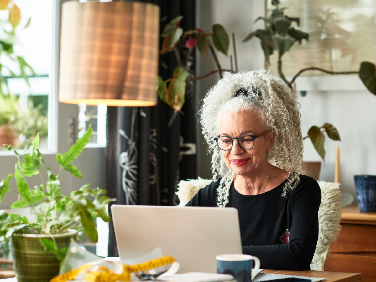 Events: Grey haired woman at home smiling in front of laptop 
