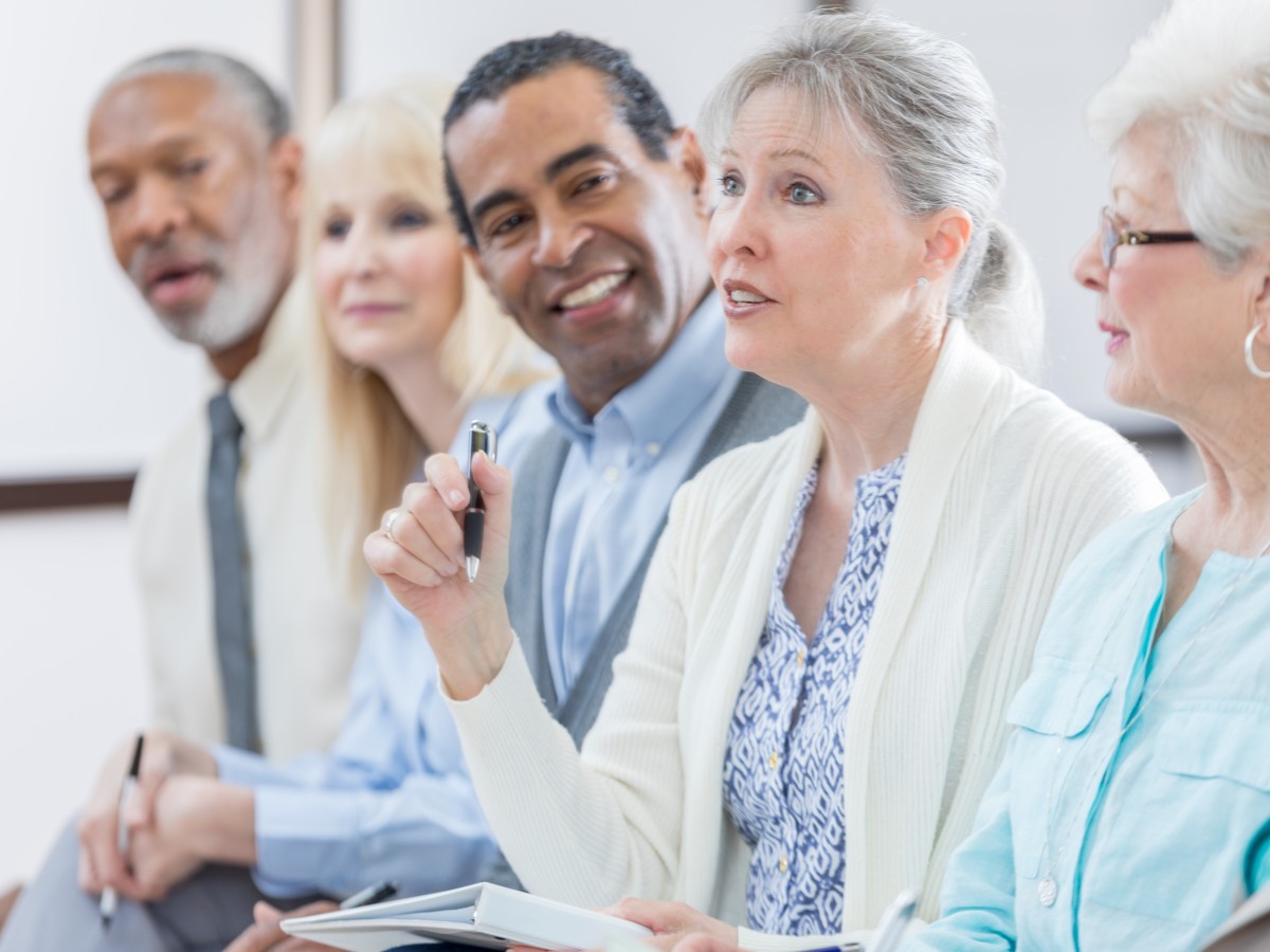 A row of seniors at an event, with one woman asking a question