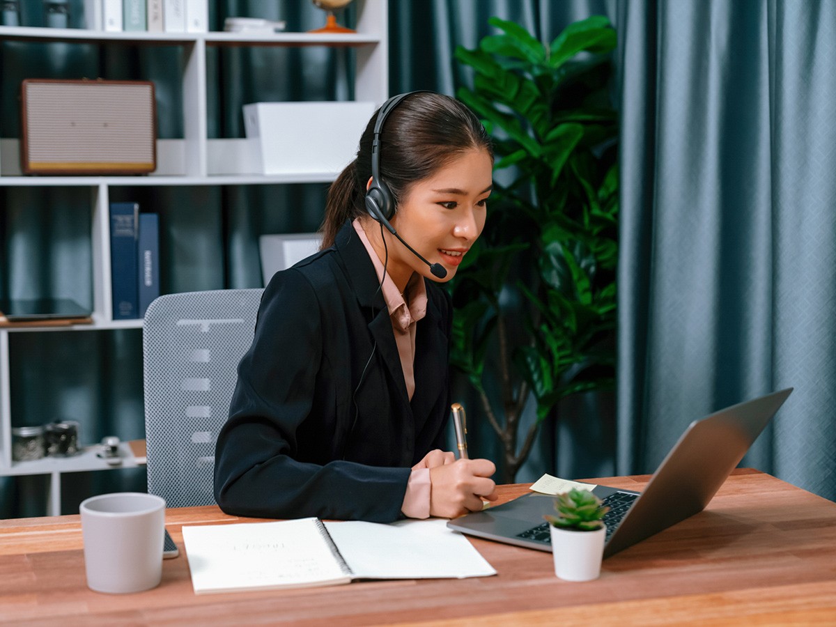 Asian woman with headset watching video conference on laptop