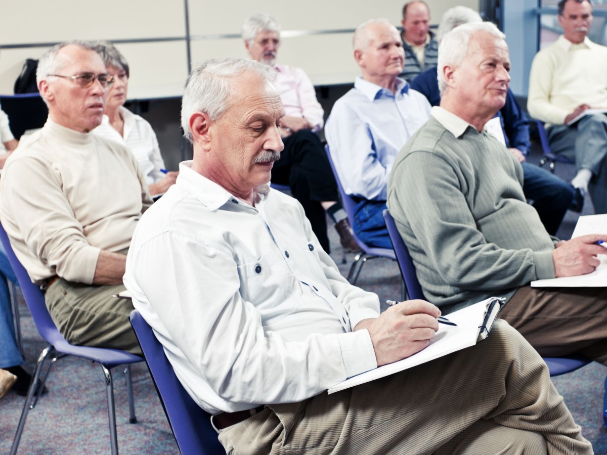 A room full of seniors, mostly men, seated in rows at a class or seminar