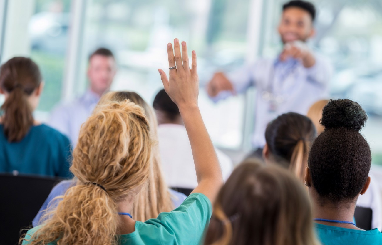 Woman in audience of a speaking event with hand up to ask a question