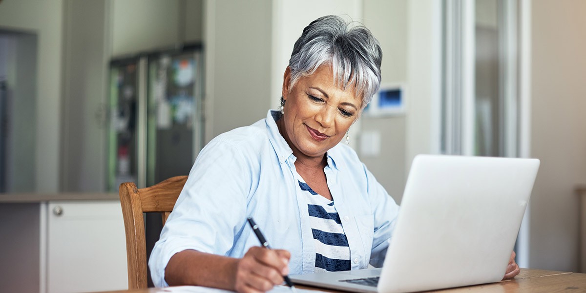 Woman writing notes on notepad while working on laptop