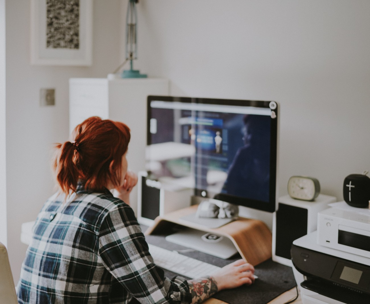 Woman in plaid shirt at desk, in front of large computer display