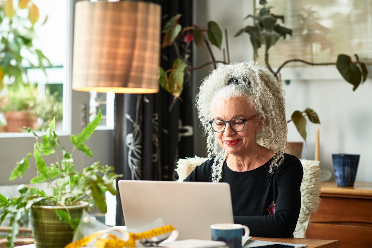 Events: Grey haired woman at home smiling in front of laptop 