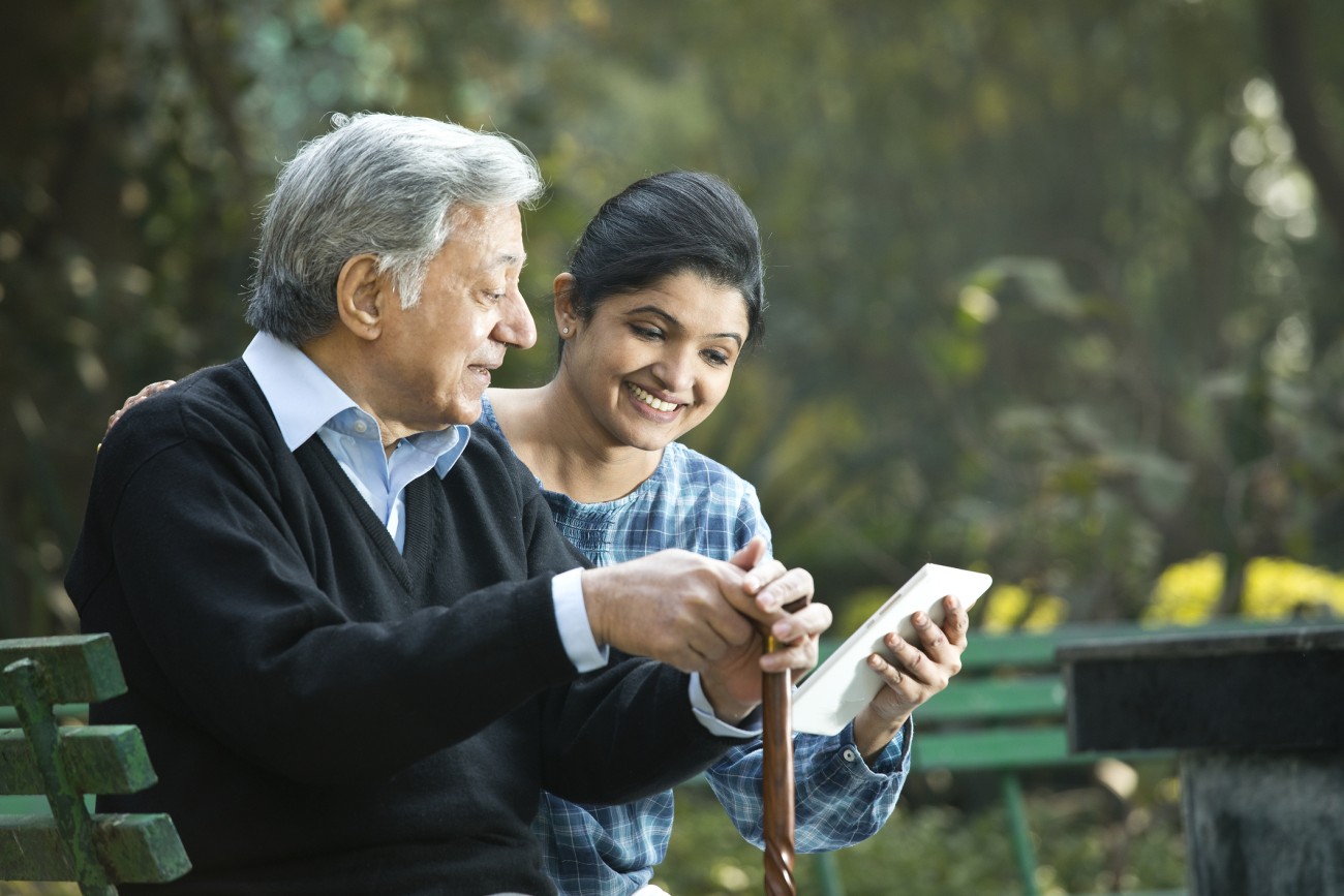 South Asian senior man watching webinar on tablet held by young woman