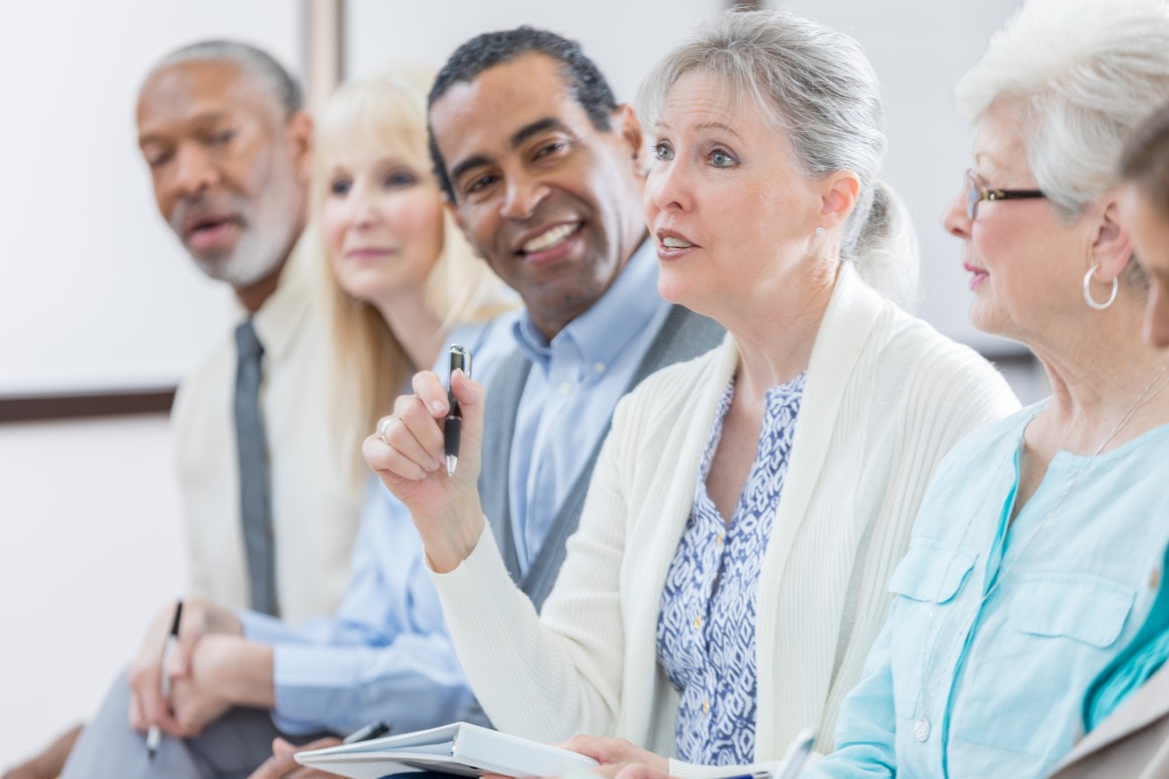 A row of seniors at an event, with one woman asking a question