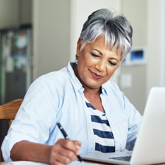 Woman writing notes on notepad while working on laptop