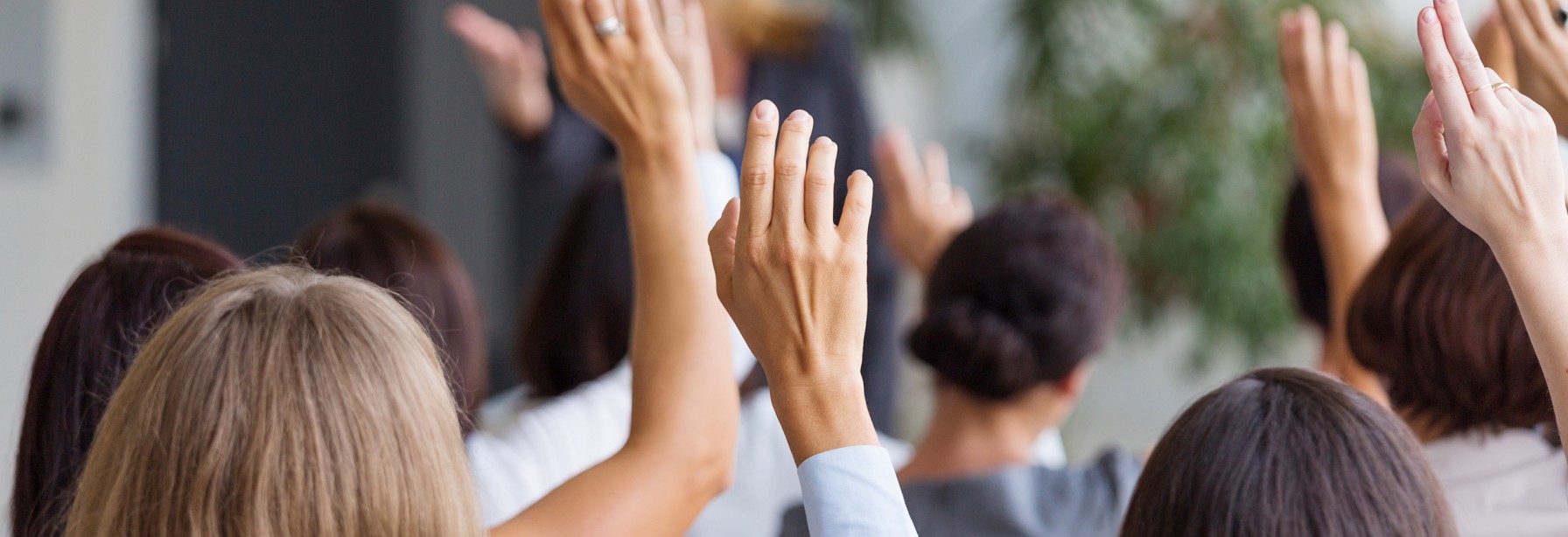 Crowd of people holding their hands up to ask a question