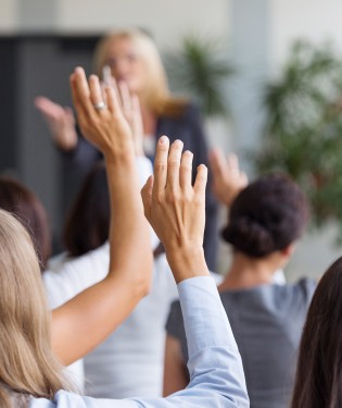 Crowd of people holding their hands up to ask a question