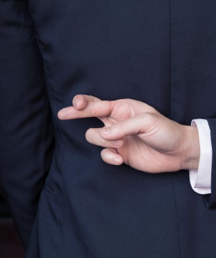 Man in suit stands with fingers crossed behind his back.